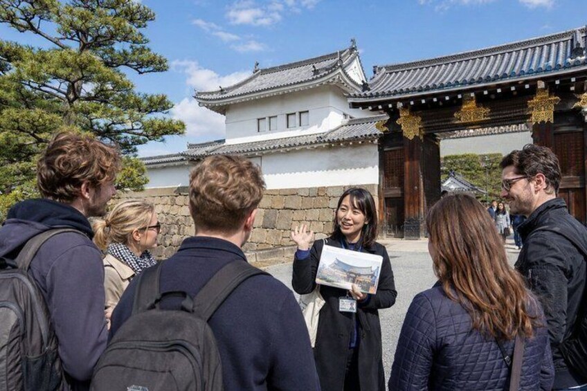 A group of tourists standing in front of a traditional Japanese gate with a white building in the background. 1