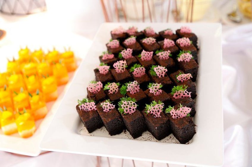 A white rectangular plate with neatly arranged chocolate squares topped with pink and green decorations. 5