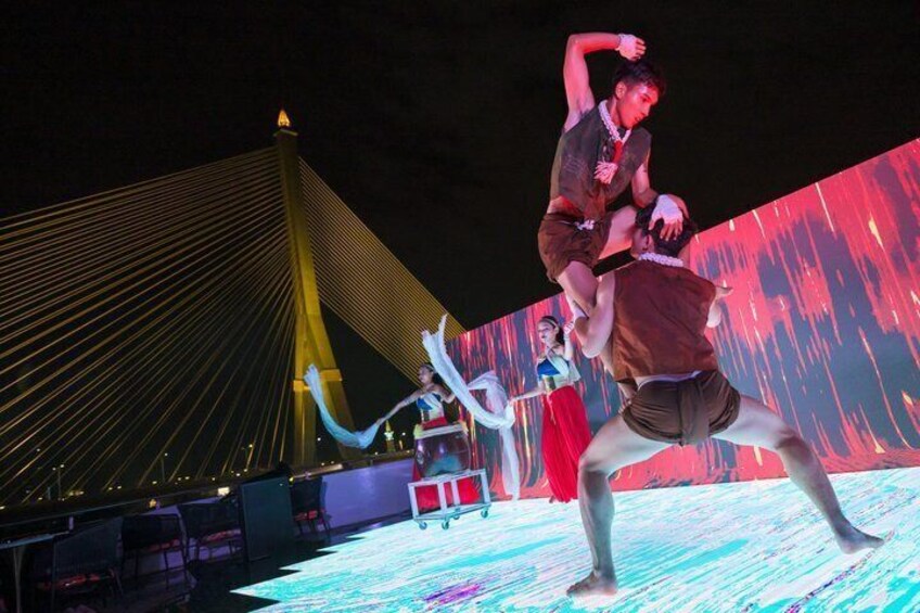 A nighttime outdoor performance with dancers on a stage, a large illuminated screen in the background, and a bridge structure. 4