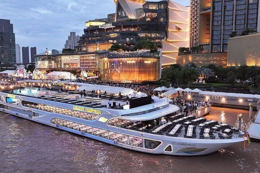 A river cruise boat with dining areas and a cityscape in the background. 2