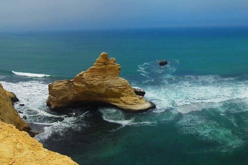 A coastal landscape with a prominent rock formation near the water's edge. 5