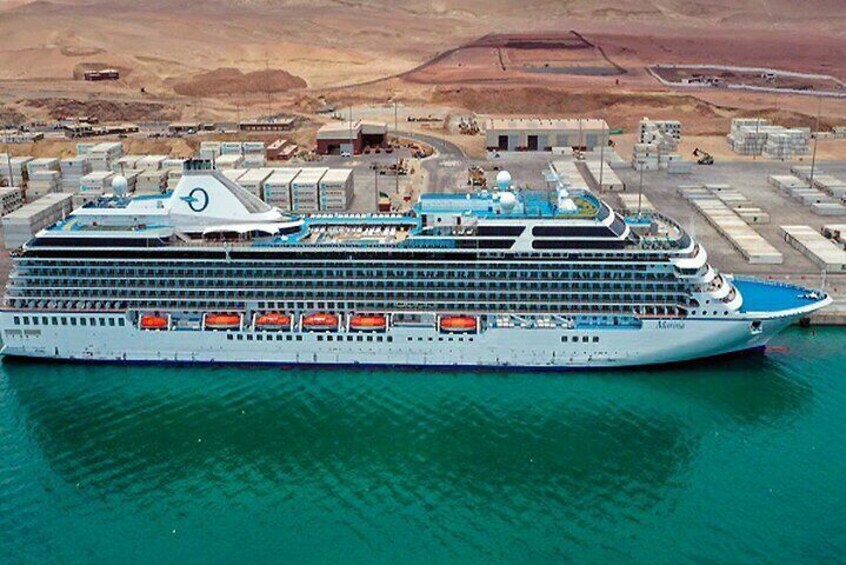 A large cruise ship docked at a port with a desert landscape in the background. 1