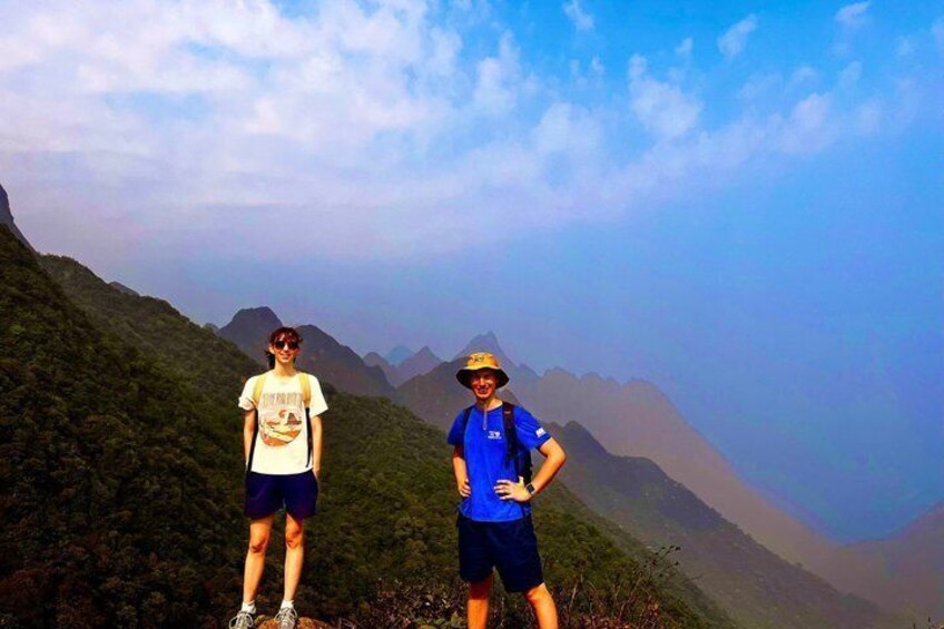 Two people standing on a mountain with a clear sky and distant mountains in the background. 1