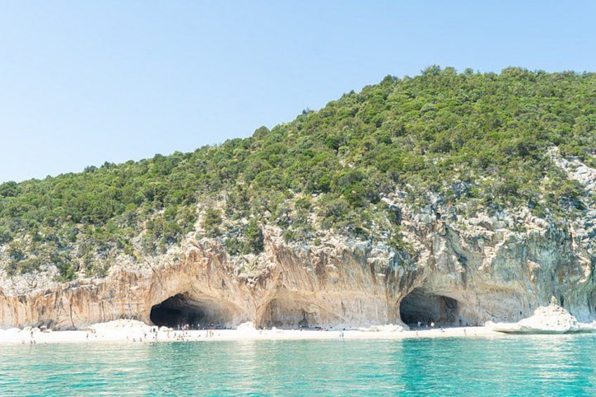 A coastal landscape with a rocky cliff, a turquoise sea, and a forested hill. 4