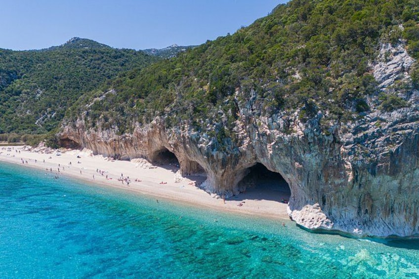 A beach with clear turquoise water, white sand, and rocky cliffs with caves. 3