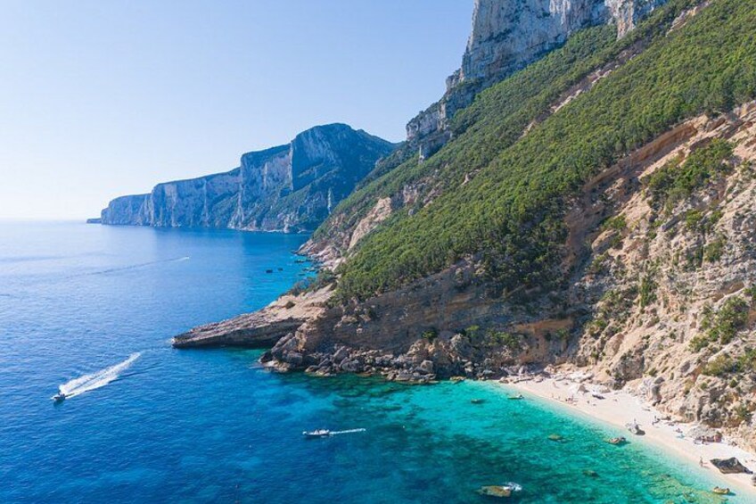 A coastal landscape with cliffs, clear blue sea, and a sandy beach. 2