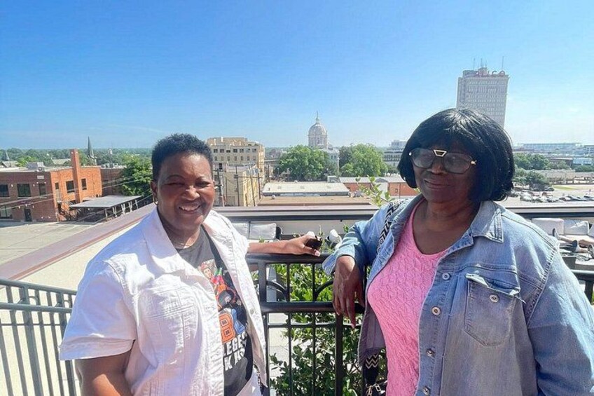 Two people standing on a rooftop with a cityscape in the background. 2