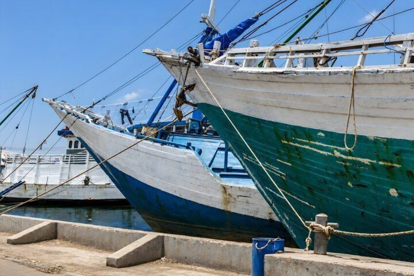 A docked fishing boat with a blue and white hull, ropes tied to a bollard, and a concrete platform. 3