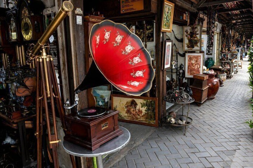 A vintage shop with antique items like a gramophone, a red umbrella, and various framed pictures. 5