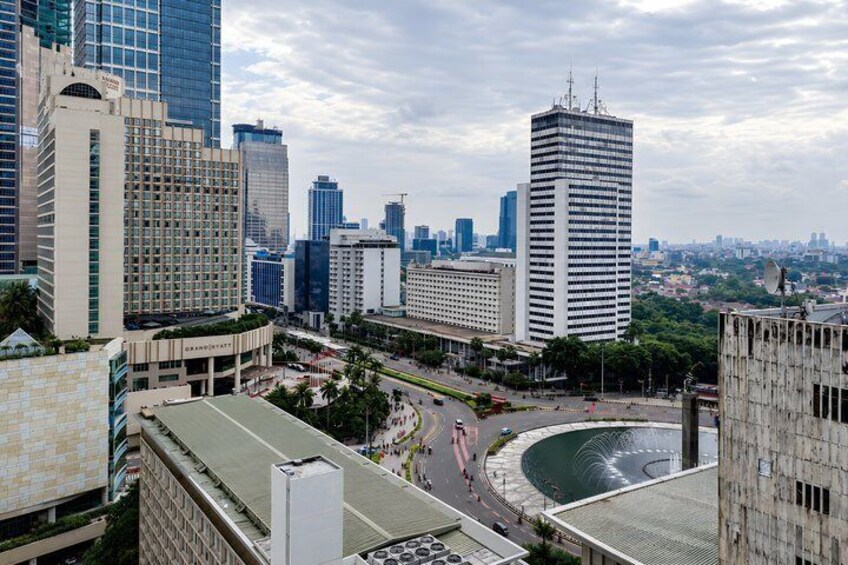 A cityscape with modern skyscrapers, a roundabout, and a fountain. 2