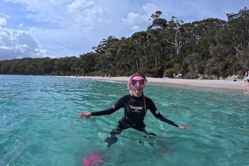 A person in a black wetsuit and pink snorkel mask swimming in clear blue water. 2