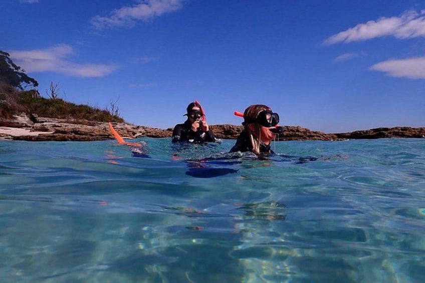 Two people snorkeling in clear blue water with rocky terrain in the background. 2