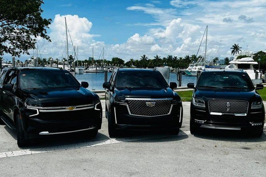 Three black SUVs parked in a lot with a marina and yachts in the background. 2