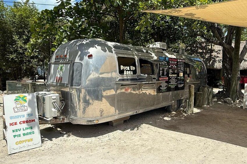 A vintage trailer with a menu board, parked in a shaded area with trees. 5