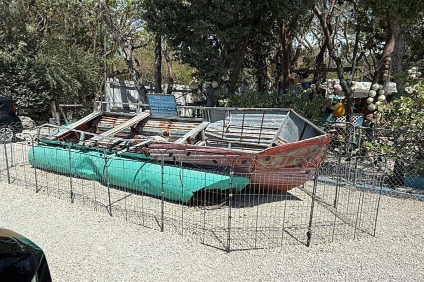 A boat on display, surrounded by a fence, with trees and a sign in the background. 3