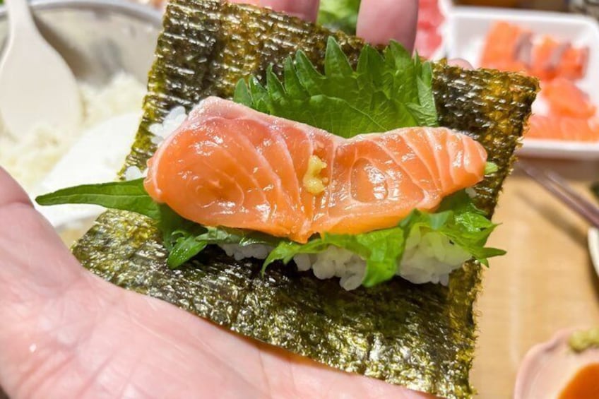 A hand holding a sushi roll with salmon and rice, garnished with green leaves. 2