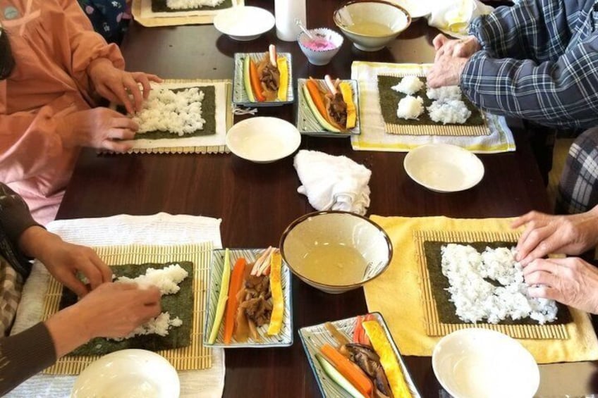 People preparing sushi at a table with various ingredients and bowls. 1