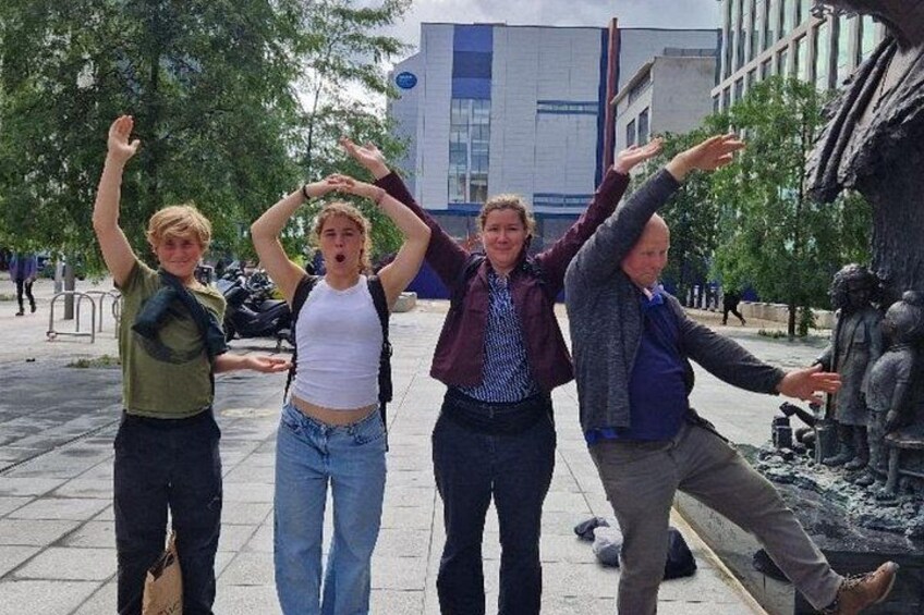 Four people posing with their arms raised in front of a sculpture. 4