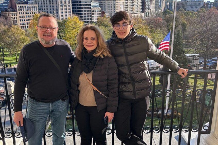 Three people standing on a balcony with a cityscape in the background. 3