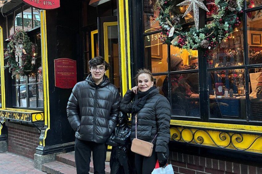 Two people standing in front of a building with yellow trim and a Christmas wreath. 5
