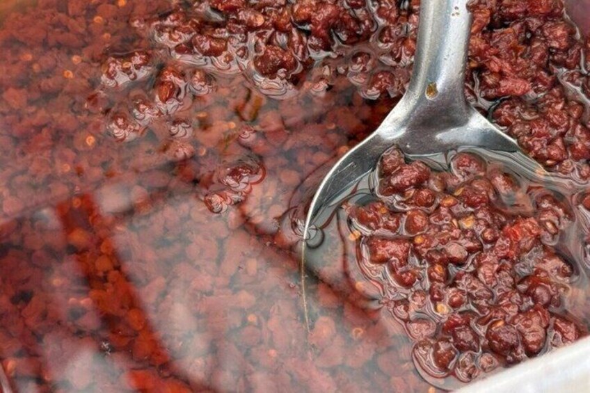 A close-up of a cooking pot with a metal spoon, containing a bubbling red liquid, likely a sauce or stew. 4