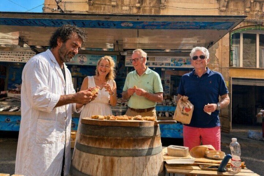 People at a street food stall with a large barrel and cooking utensils. 1