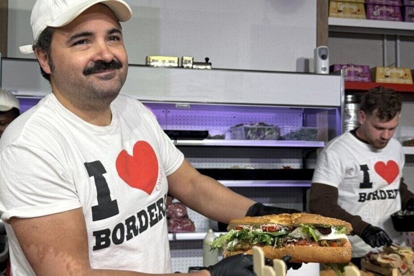 A person wearing a white t-shirt with a red heart and the text 'I love BORDEN' holding a sandwich. 2
