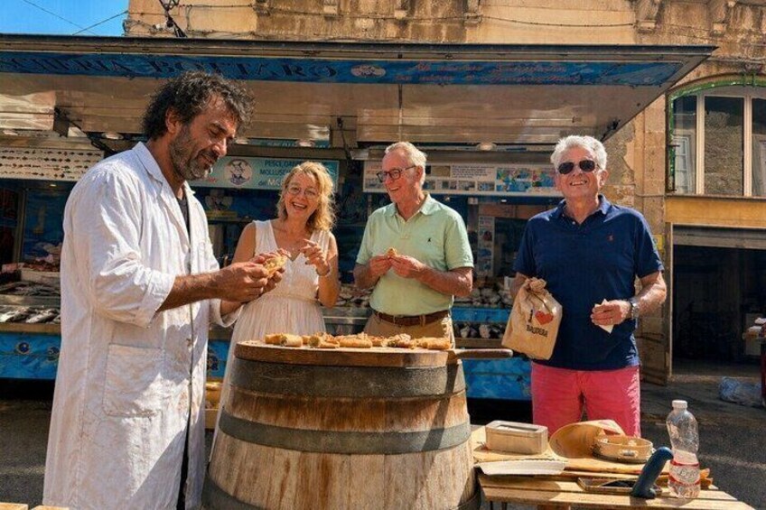 People at a street food stall with a large barrel, a woman in a white dress, and a man in a blue shirt. 1