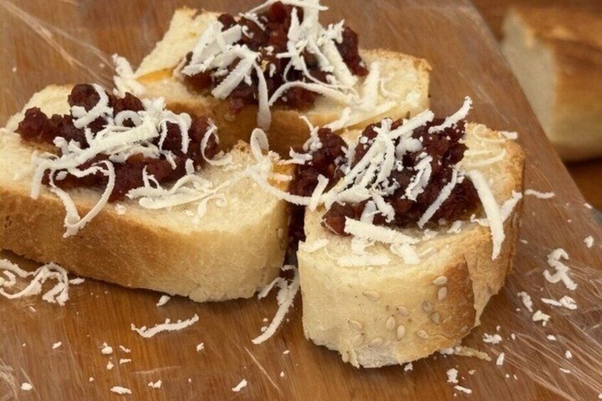 Four pieces of toast with a red spread and grated cheese on a wooden surface. 3