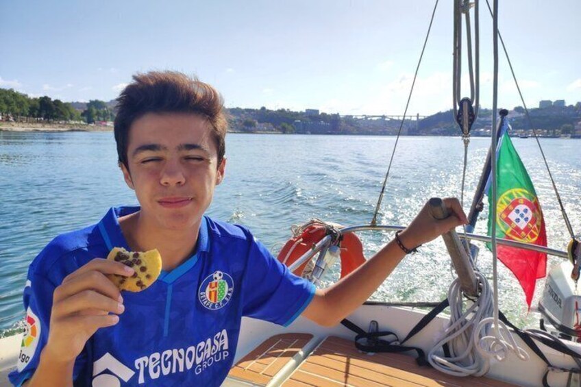 A person on a sailboat with a flag, water, and a distant shoreline. 3