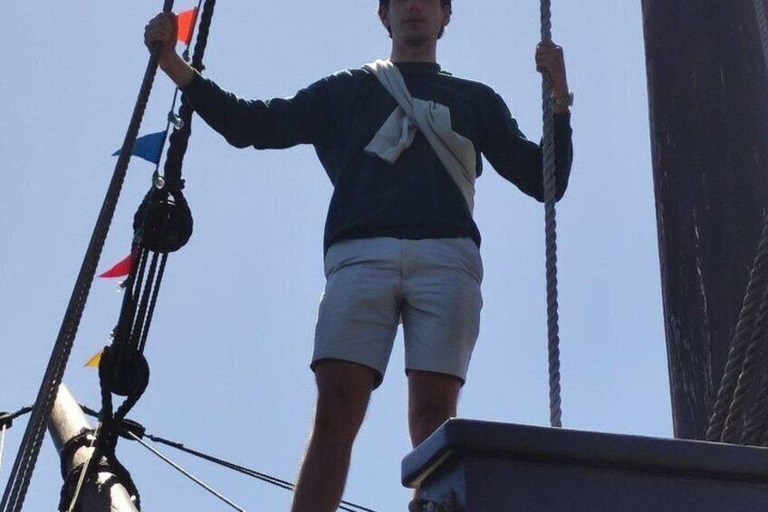 A person standing on a ship's deck, holding onto ropes. 4