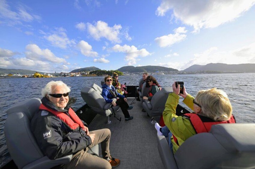 People on a boat, wearing life jackets, with a lake and mountains in the background. 5