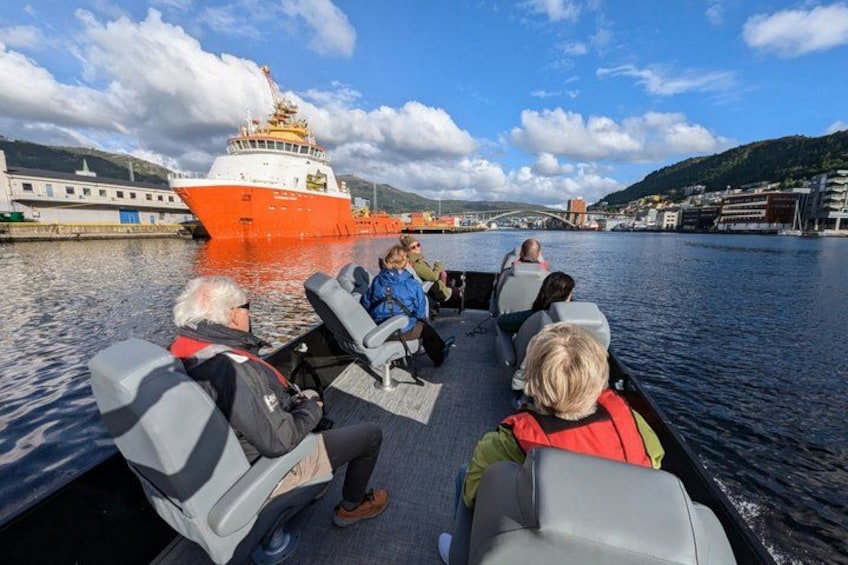 A group of people on a boat, a red ship in the background, and a bridge in the distance. 4
