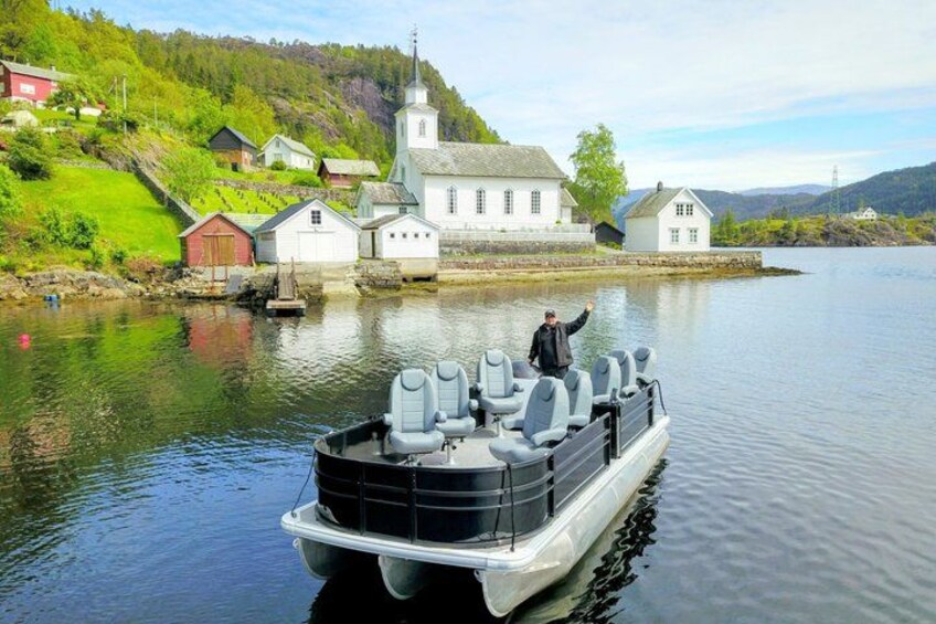 A boat with multiple seats docked near a white church and houses by a calm lake. 2