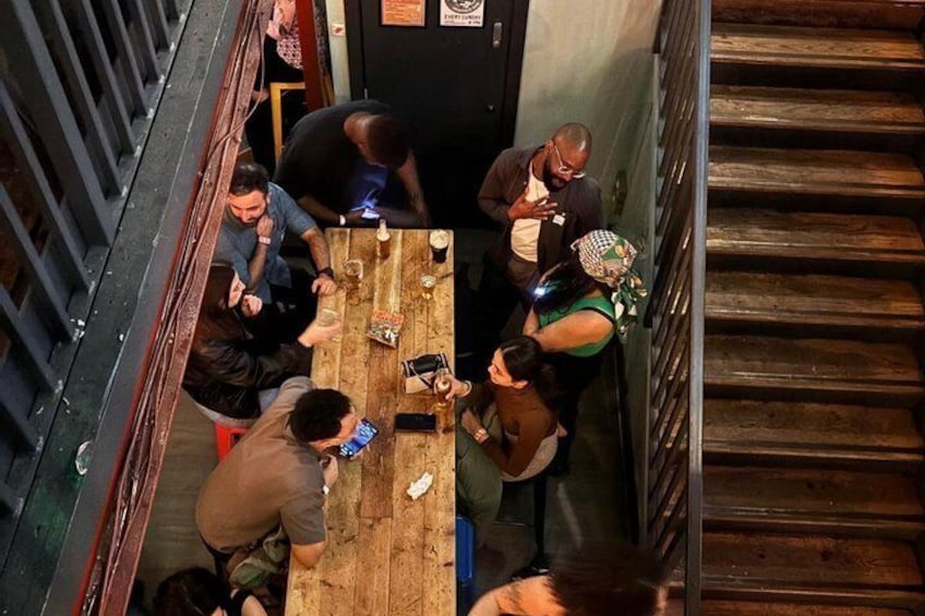A group of people sitting around a wooden table in a narrow stairwell. 3