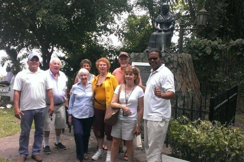 A group of people standing in a park with a statue and stone wall in the background. 1