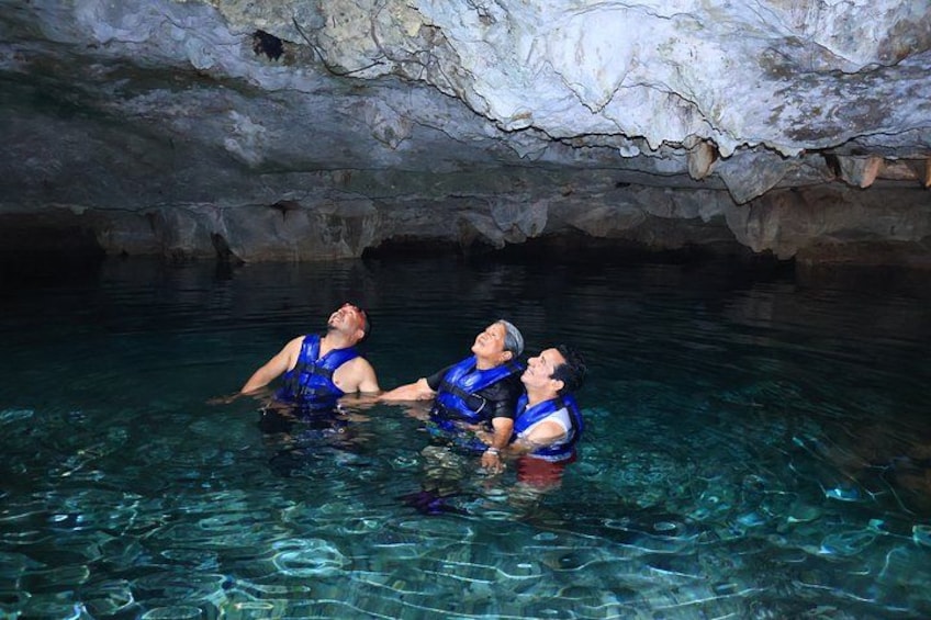 Two people in blue life jackets in a clear water body, possibly a cave or natural pool, with rocky formations overhead. 5