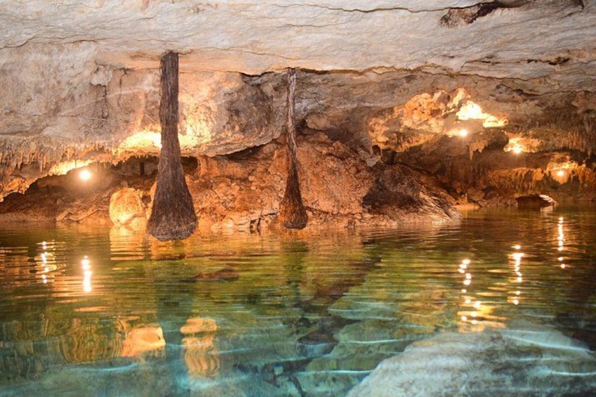 A cave with stalactites hanging from the ceiling and a pool of water at the bottom. 1