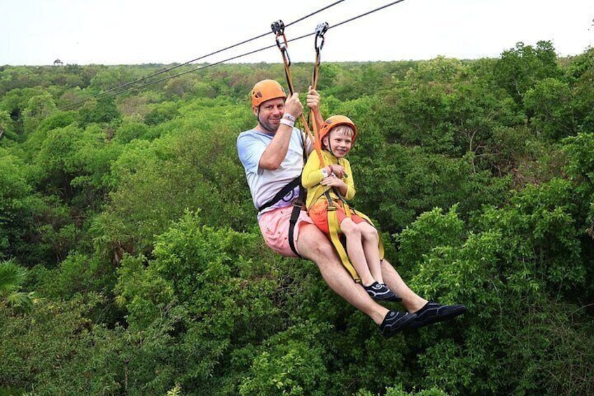 A person and a child on a zipline, surrounded by dense green foliage. 5