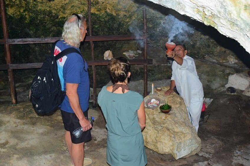 A cave with a ritualistic setup, including a person performing a ceremony with smoke, a table with offerings, and a group of onlookers. 2