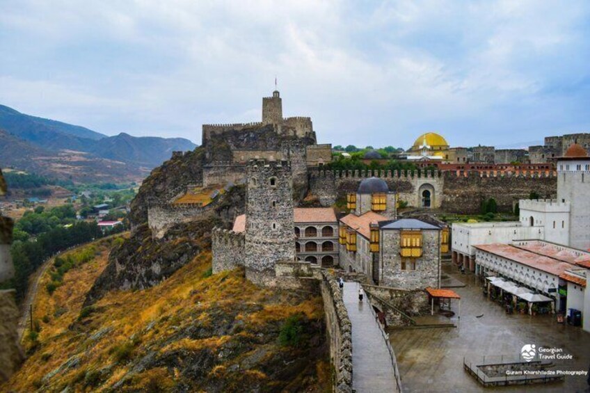 A historic stone fortress with a prominent tower, a yellow-domed building, and a surrounding landscape. 4