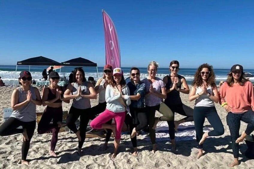 A group of people performing a synchronized dance on a sandy beach with tents and a flag in the background. 5
