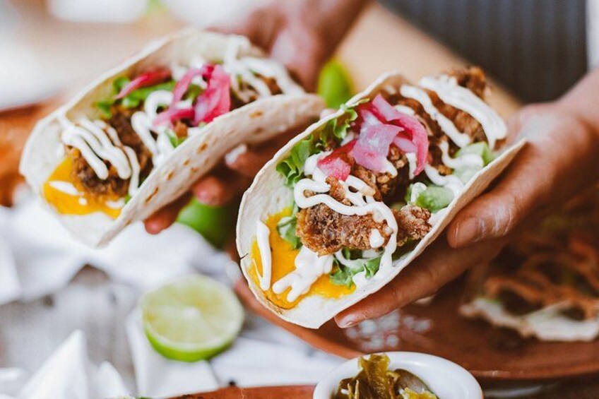 Two tacos with meat, lettuce, and a white sauce, held by hands. 1