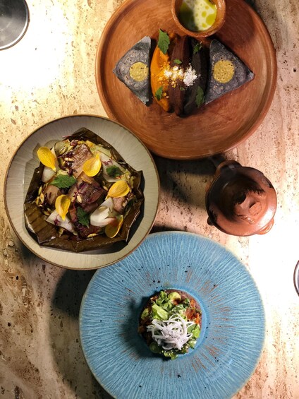 A table with three dishes: a meat dish with vegetables, a bowl with a yellow sauce, and a blue plate with a green topping. 3