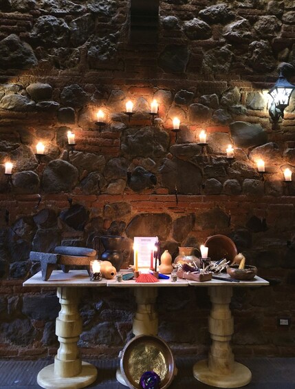 A stone wall with lit candles and a table with various objects. 1
