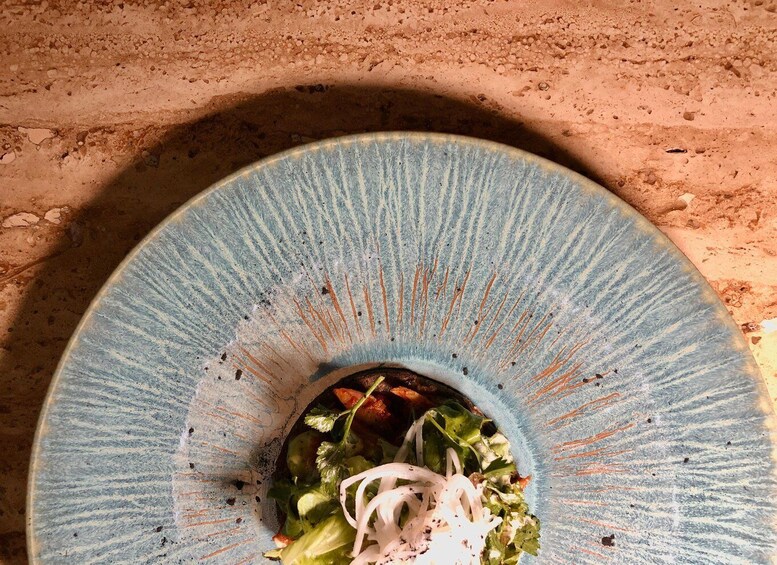 A blue ceramic bowl with a rustic texture, filled with a salad including greens and onions, on a sandy surface. 4