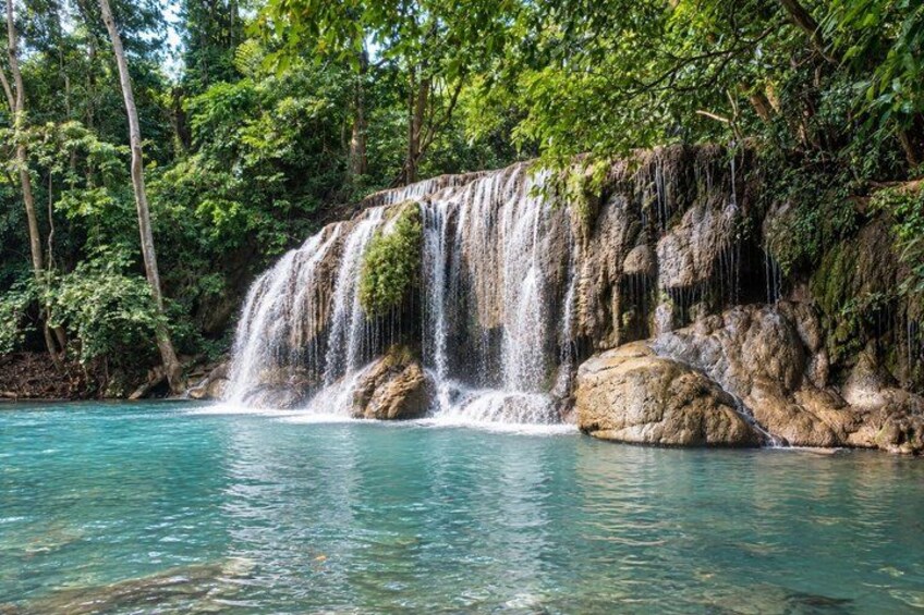 A waterfall cascading over rocks into a clear blue pool surrounded by lush greenery. 1