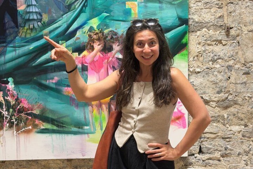 A person pointing at a colorful painting with a stone wall in the background. 1