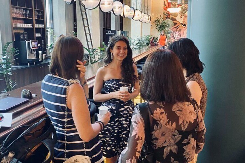 A group of people conversing in a cafe with a coffee machine and plants in the background. 5