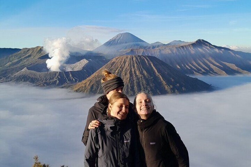 Two people standing in front of a volcano with smoke and clouds. 1